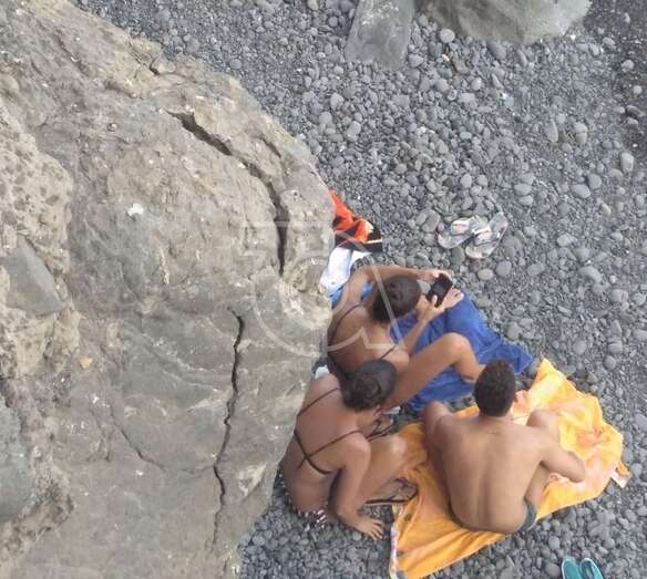 Tres jóvenes en una pequeña cala de callaos debajo de una roca agrietada en los riscos de Salinetas/TA.